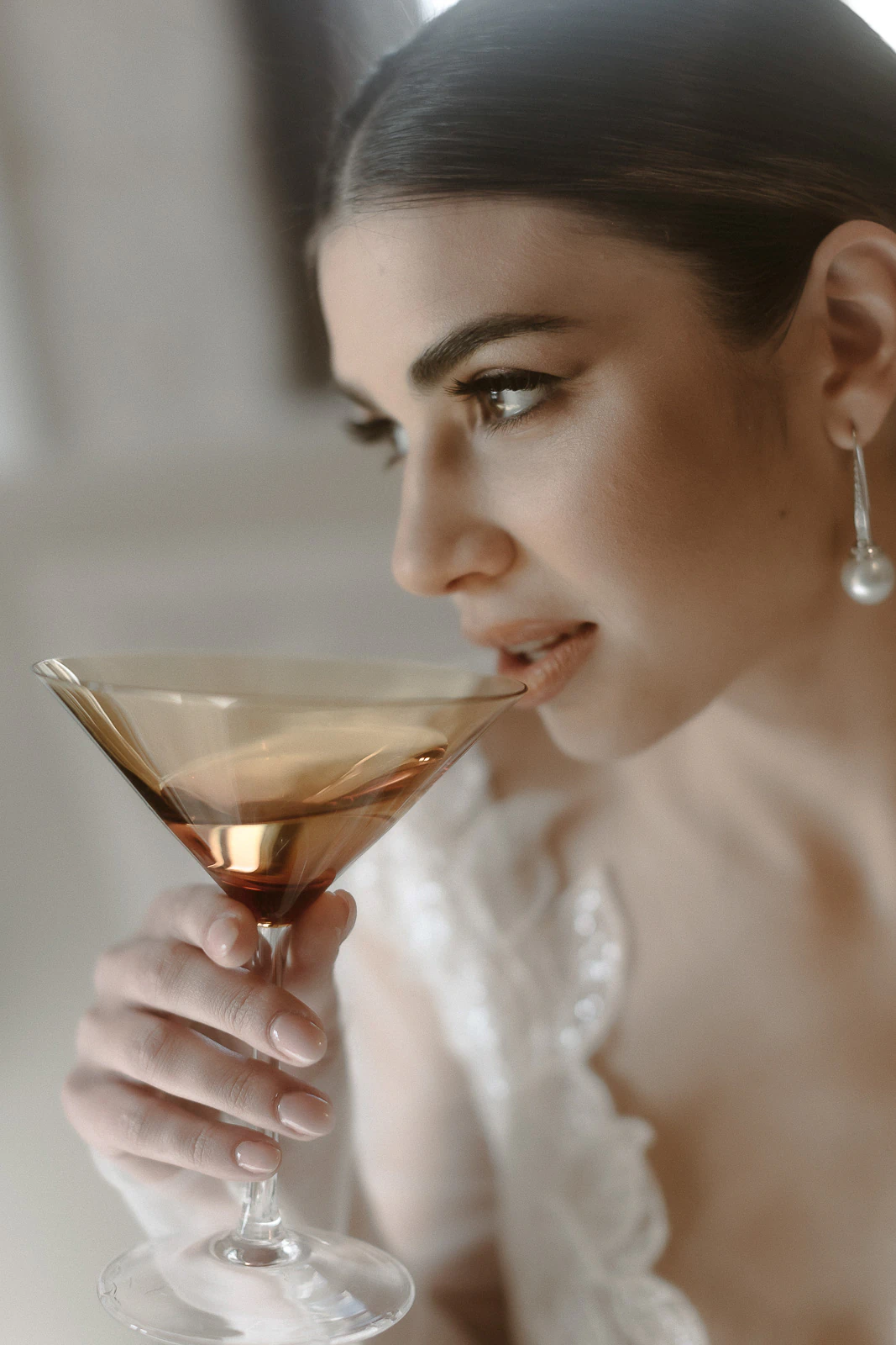 In Puglia, a woman with pearl earrings savors a crafted cocktail, her elegant touch reflecting the region’s refined celebration.