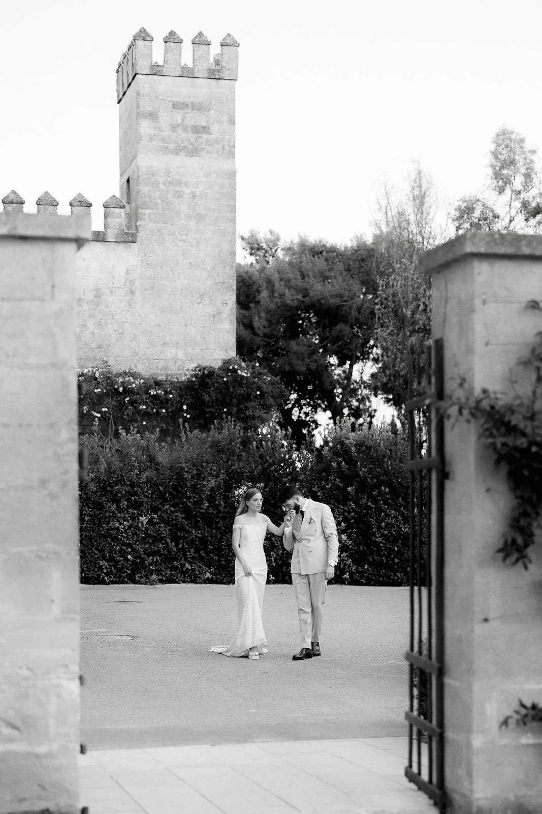 A bride and groom share a quiet moment by an ancient stone tower and lush greenery at a romantic wedding in Puglia, Italy.