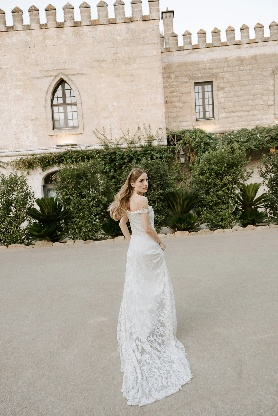 A bride in lace glances back, framed by the storied stone architecture of Puglia, Italy—a moment of timeless romance.