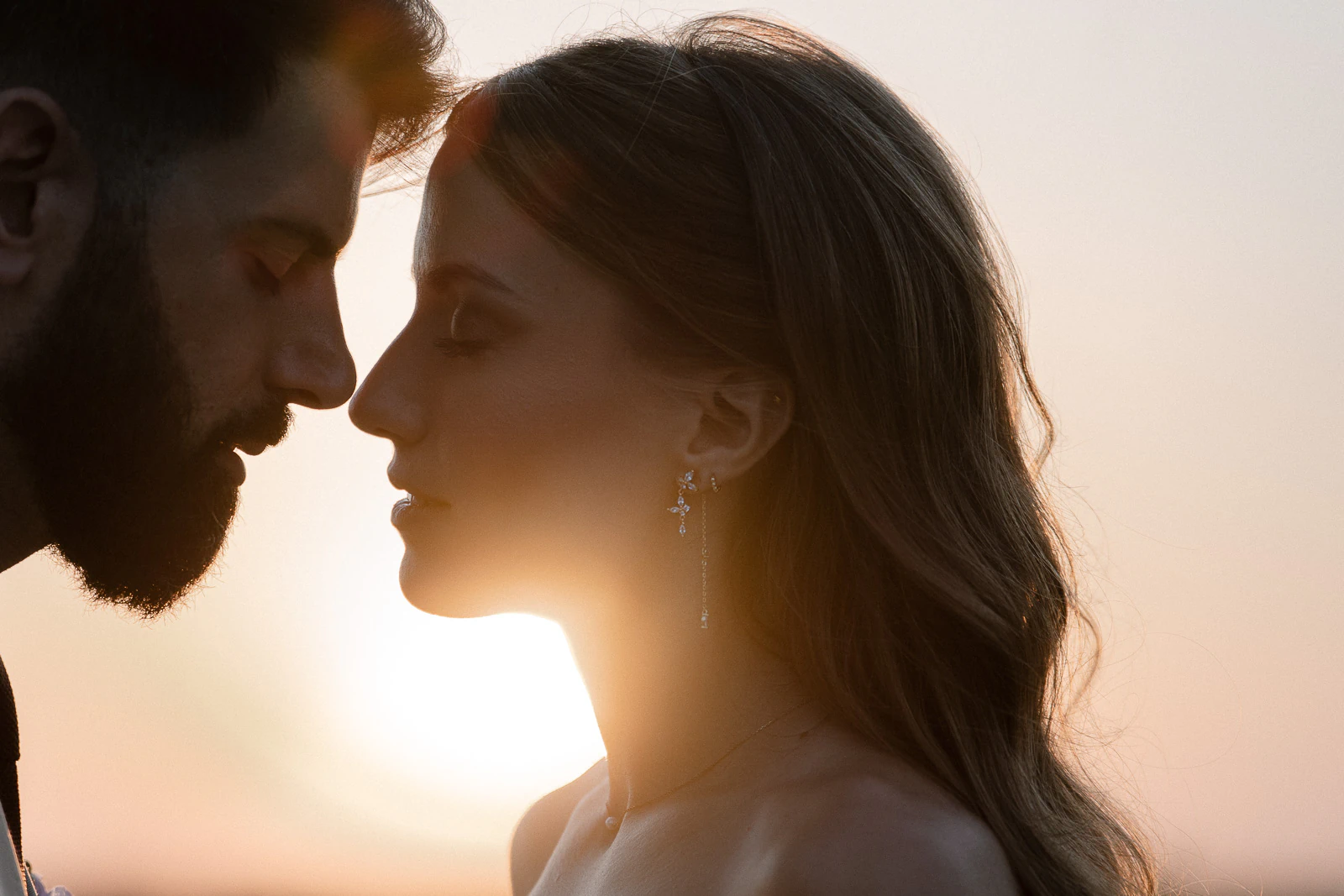 Bathed in golden Puglian light, a couple share an intimate sunset moment, eyes closed in tender anticipation.