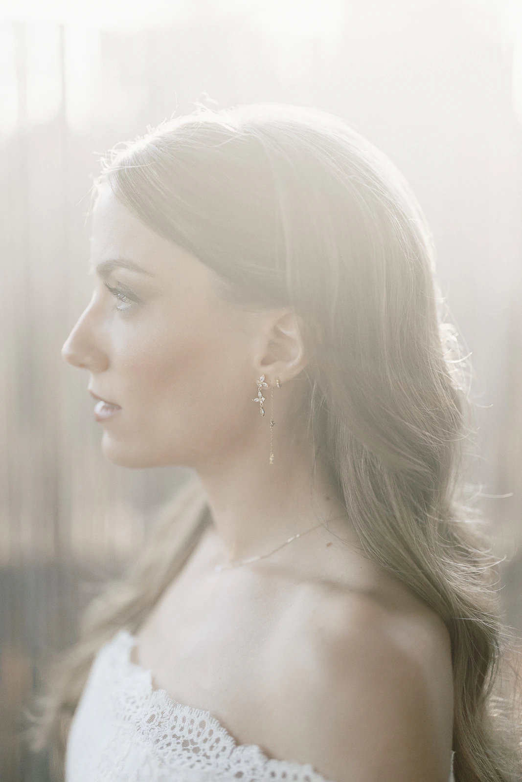 Elegant bride in off-shoulder lace, softly illuminated in profile, embraces serene romance amidst sunlit Puglia, Italy.
