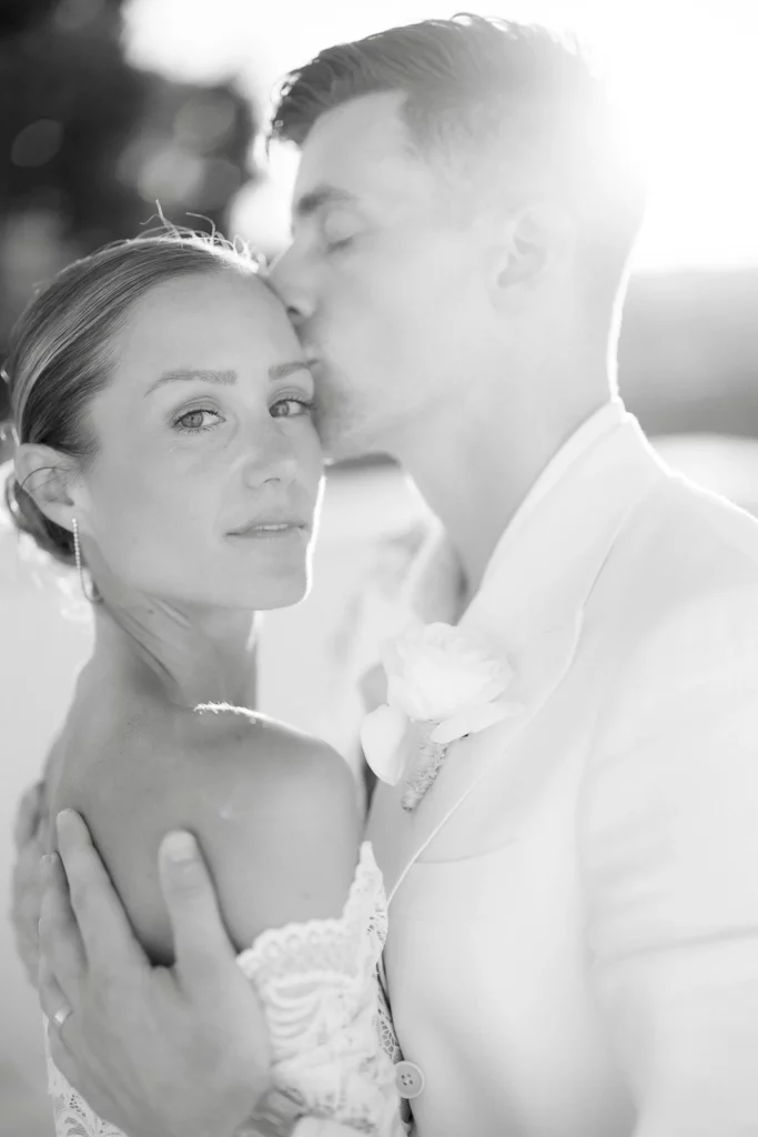 In sunlit Puglia, a groom in a pale suit tenderly kisses his bride’s forehead, radiating romance and effortless Italian elegance.