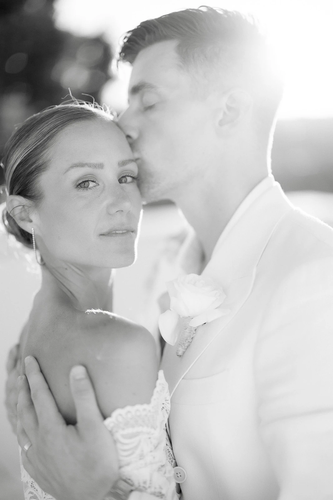 In sunlit Puglia, a groom in a pale suit tenderly kisses his bride’s forehead, radiating romance and effortless Italian elegance.