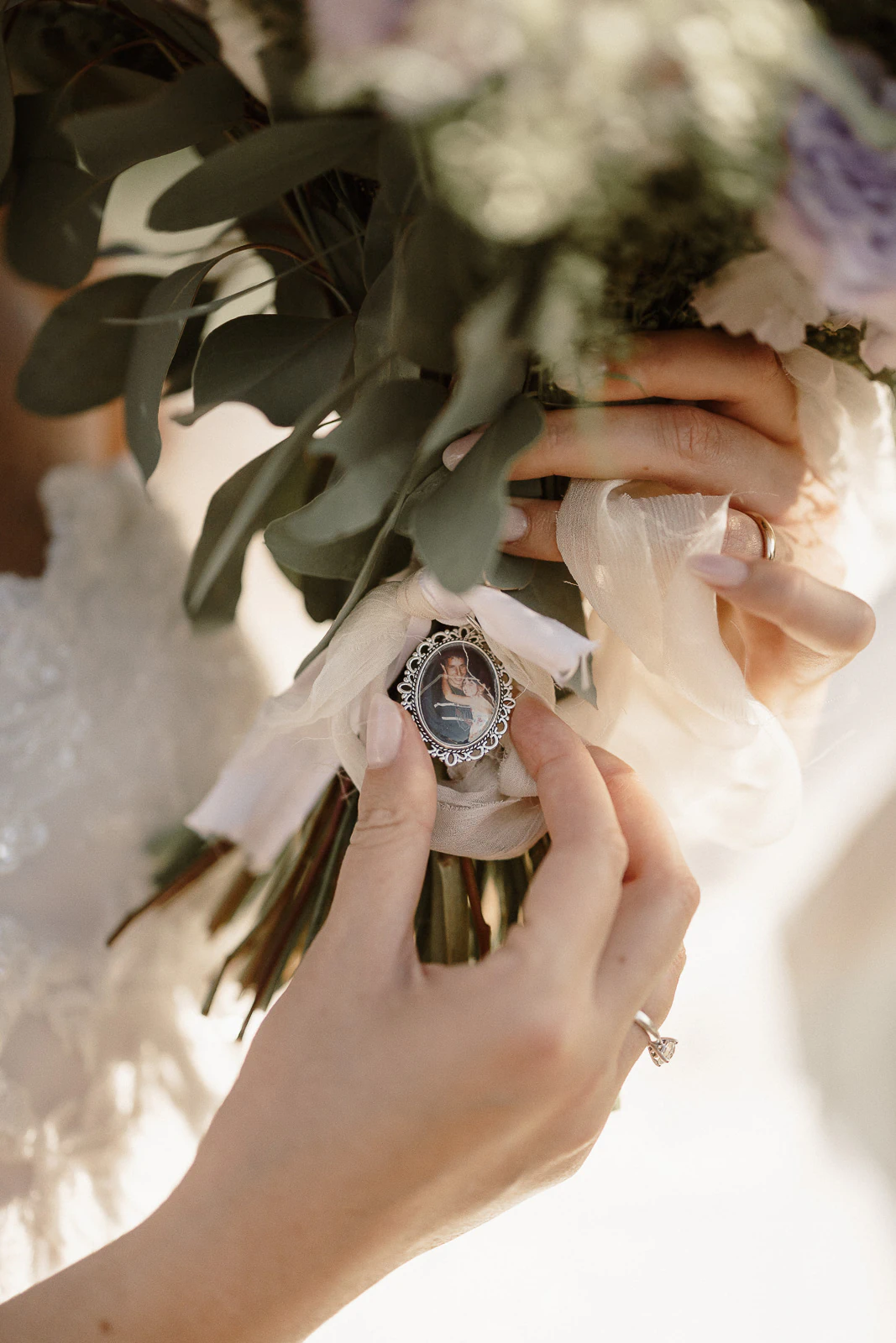 A close-up of a bride in Puglia tenderly clutching her bouquet, adorned with silk ribbon and a cherished photo charm.