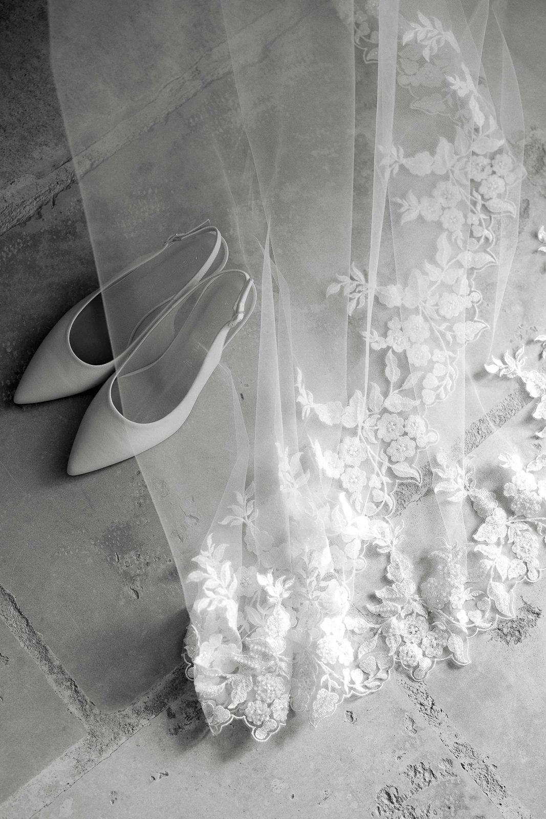 White pointed heels rest beside a delicate floral veil, illuminated on sun-warmed stone in a romantic Puglian setting.
