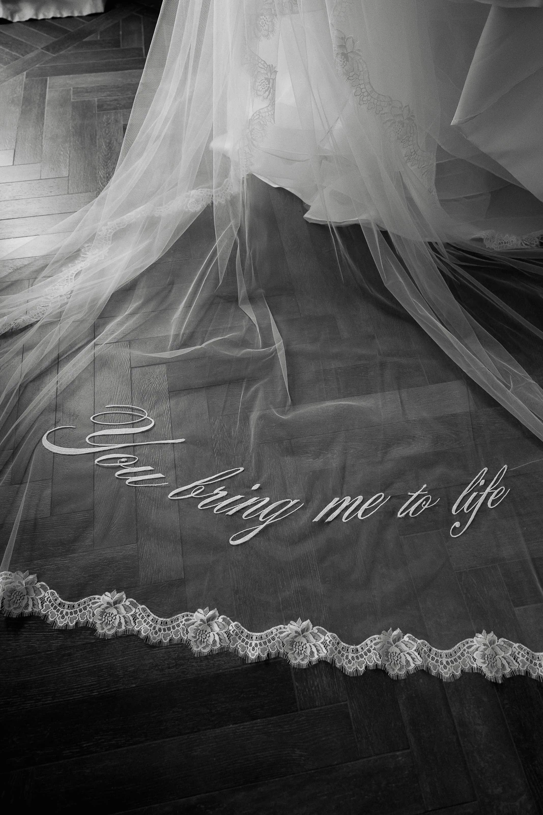 In Puglia, a lace-trimmed bridal veil lies elegantly on wood, delicately embroidered with You bring me to life.