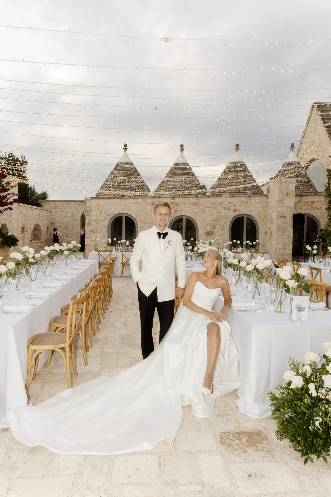 Amidst Puglia’s sunlit stone architecture, a bride and groom share an intimate moment at their elegant outdoor reception.