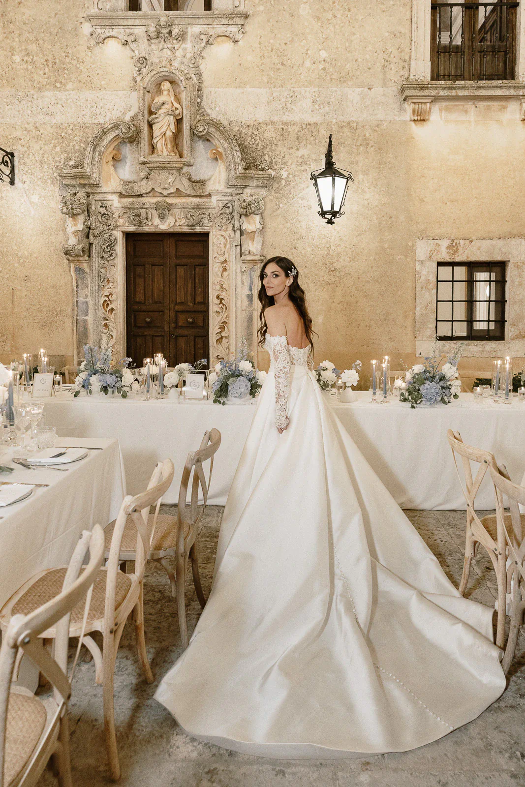 A radiant bride lingers amidst candlelit banquet tables in a romantic Puglia courtyard, framed by historic Italian architecture.
