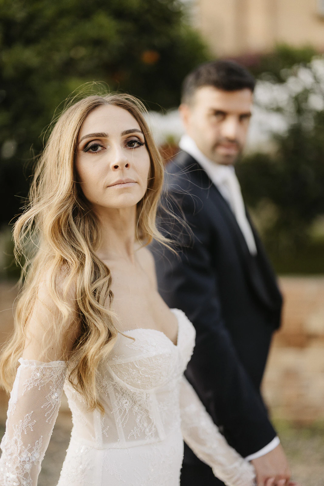 In the golden light of Puglia, a serene bride in lace shares an intimate moment with her groom amidst sun-drenched scenery.