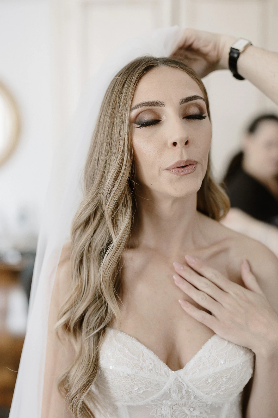 In sunlit Puglia, a serene bride in a white strapless gown has her veil gently arranged before the ceremony.