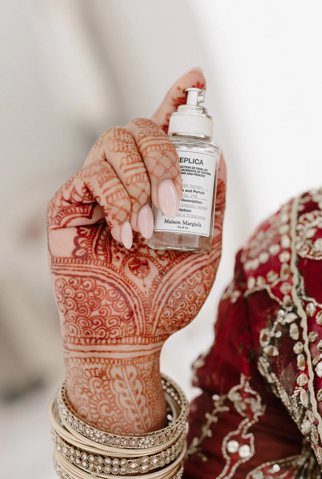 In sun-drenched Puglia, a henna-adorned hand holds Replica perfume, gold bangles shimmering above exquisite red embroidery.