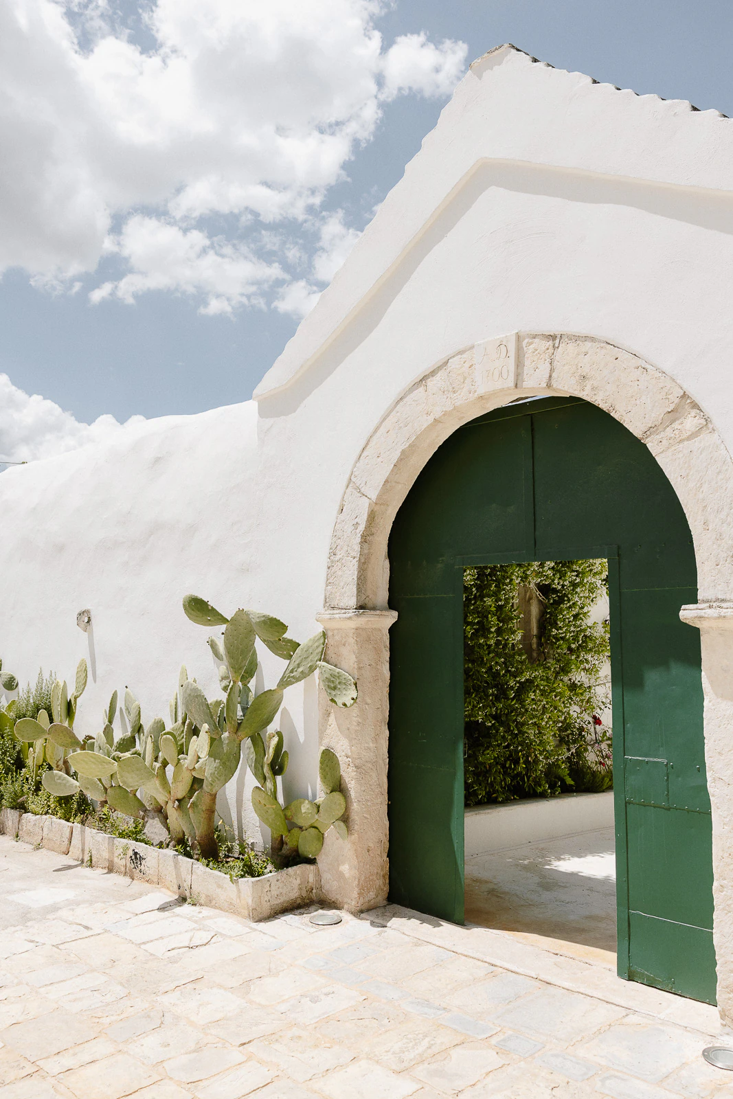 Elegant Puglia villa with white stucco, arched green doorway and cacti, perfect for a romantic Italian destination wedding.