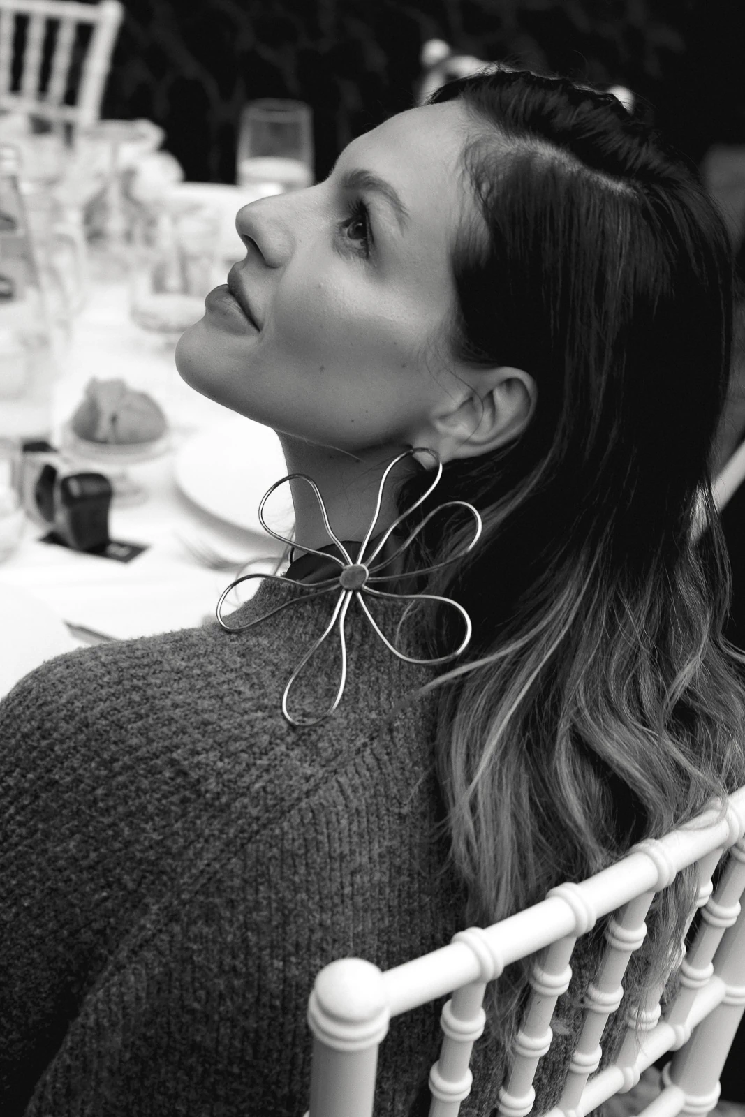 In Puglia, a contemplative woman gazes upward at an elegant wedding table, her floral earring evoking timeless Italian romance.