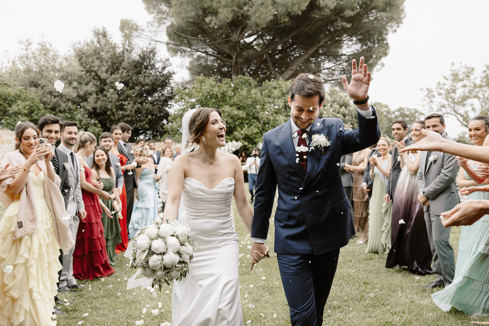 In Puglia, a joyful bride and groom stroll hand in hand through petals, embraced by the warmth of loved ones.
