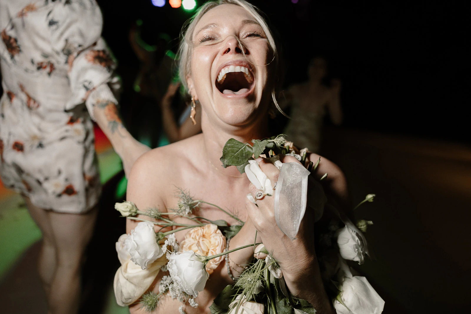 Amid joyous celebration in Puglia, a woman in a strapless gown laughs, clutching pale blooms beneath the Italian sun.
