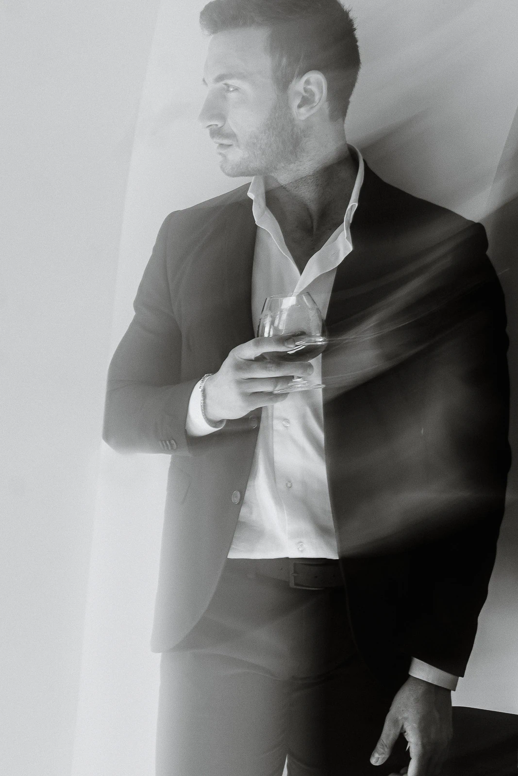 A groom in a tailored suit gazes thoughtfully in Puglia, captured in cinematic black and white with soft streaks of light.