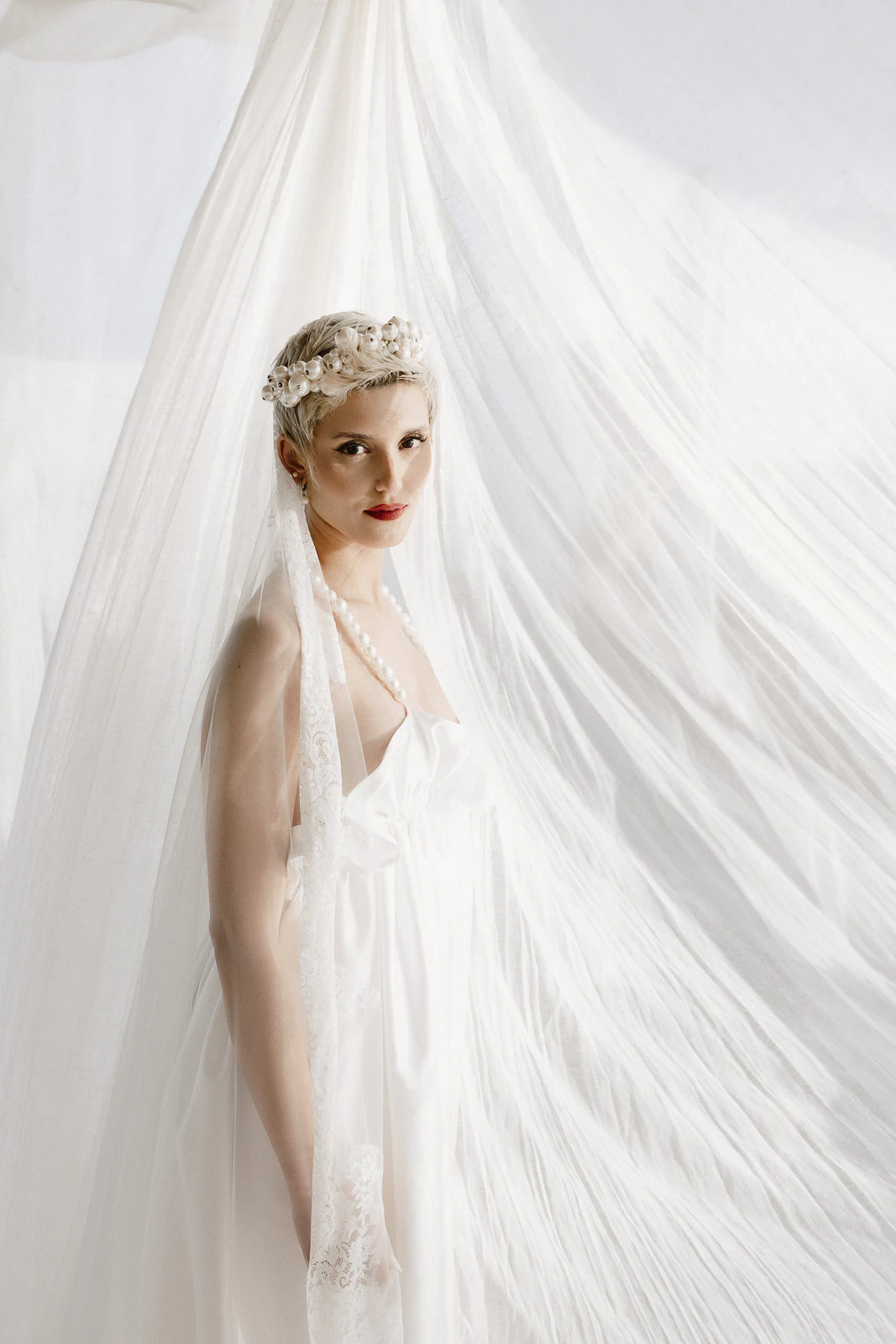 A bride in an ethereal white gown and floral crown stands before billowing drapes, embodying Puglia’s romantic elegance.