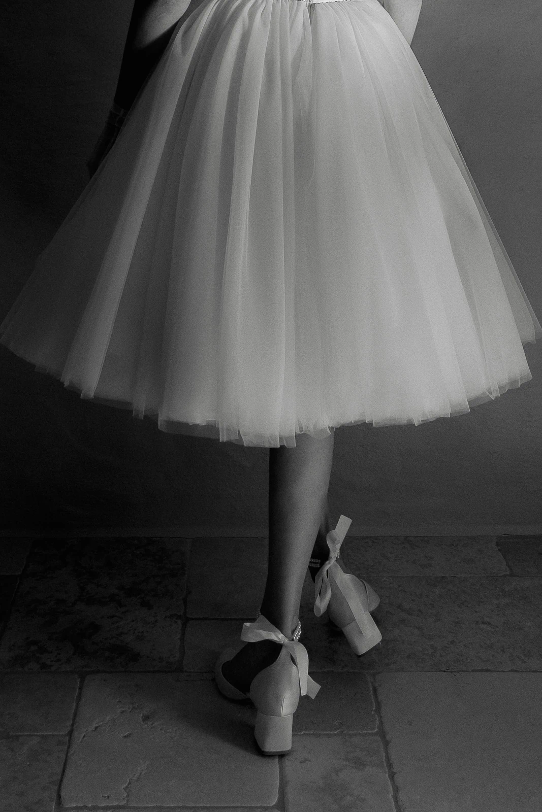 Graceful in a tulle dress and elegant heels, a guest’s poised steps echo through sunlit tiles of a Puglian wedding.