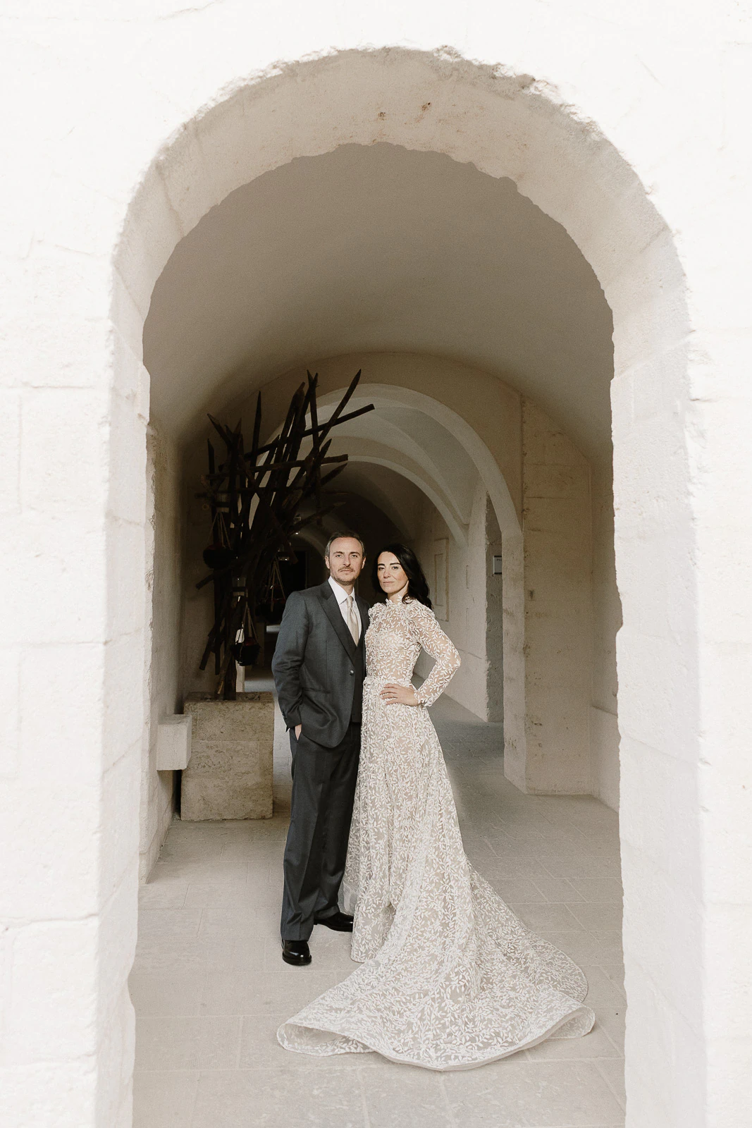 Embracing beneath a historic stone archway in Puglia, an elegant couple radiates intimacy and refined Italian wedding style.