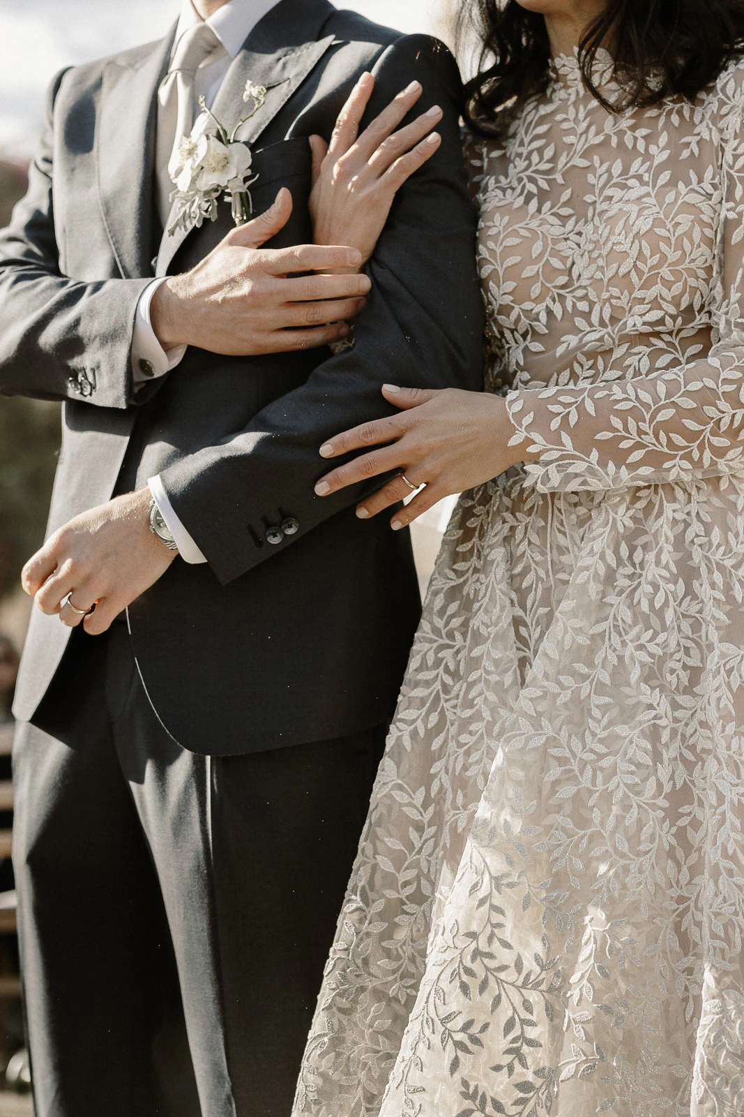 Amid Puglia’s timeless charm, a bride in floral lace and her groom share an intimate moment, wedding bands gleaming.