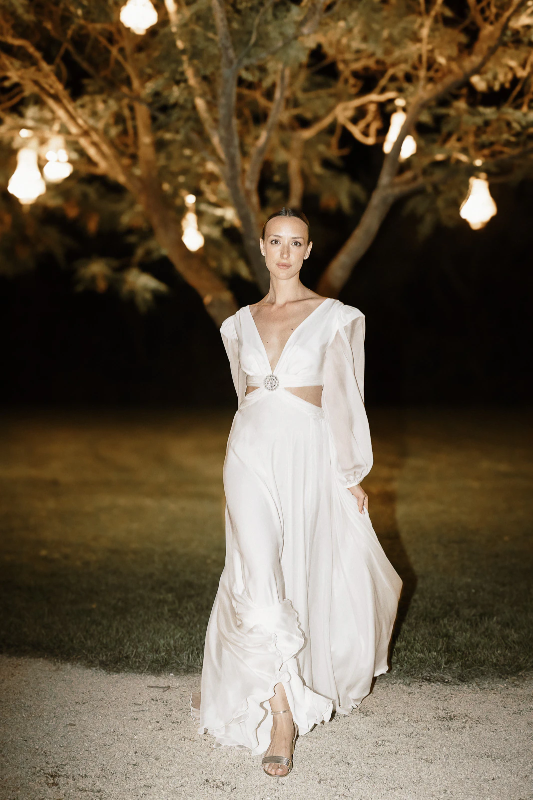 A bride in a flowing white gown strolls under glowing lights in Puglia, embraced by the enchanting Italian night.