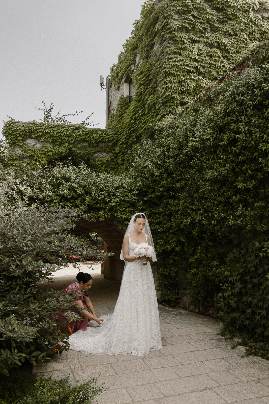 In a sunlit Puglia garden, a bride’s gown is lovingly arranged amid ivy-clad walls and timeless Italian romance.