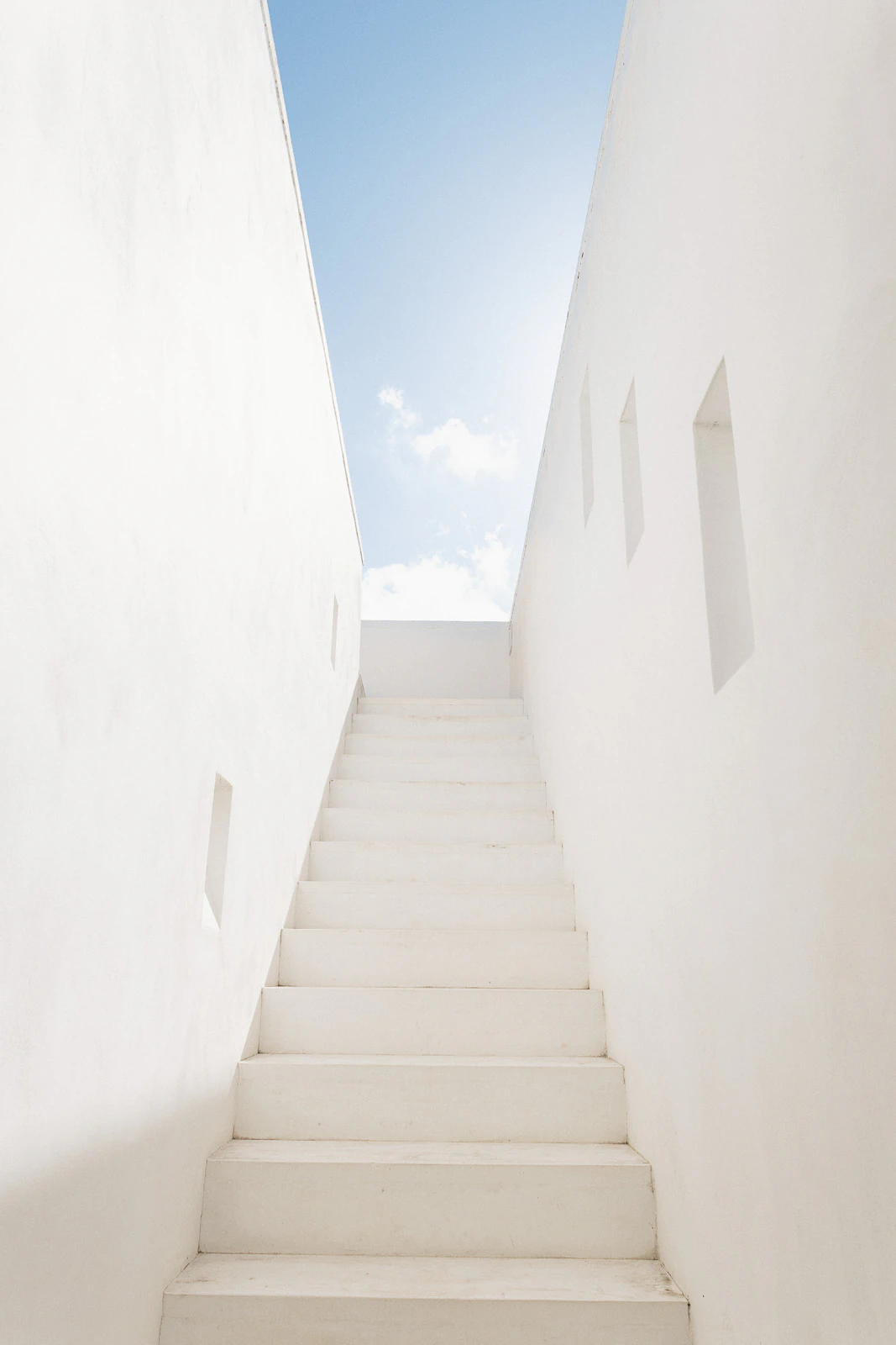 Sunlit white stone stairs in Puglia ascend between elegant walls toward a luminous Italian sky, inviting romance and celebration.