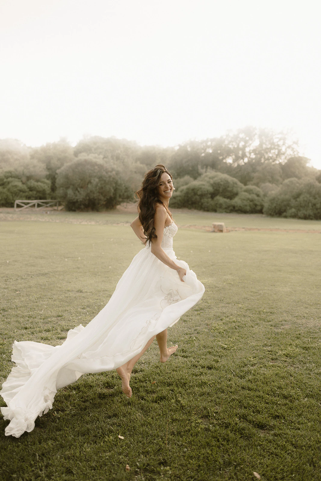 A bride in an elegant white gown runs barefoot through sunlit fields, embraced by Puglia’s natural beauty and romantic atmosphere.