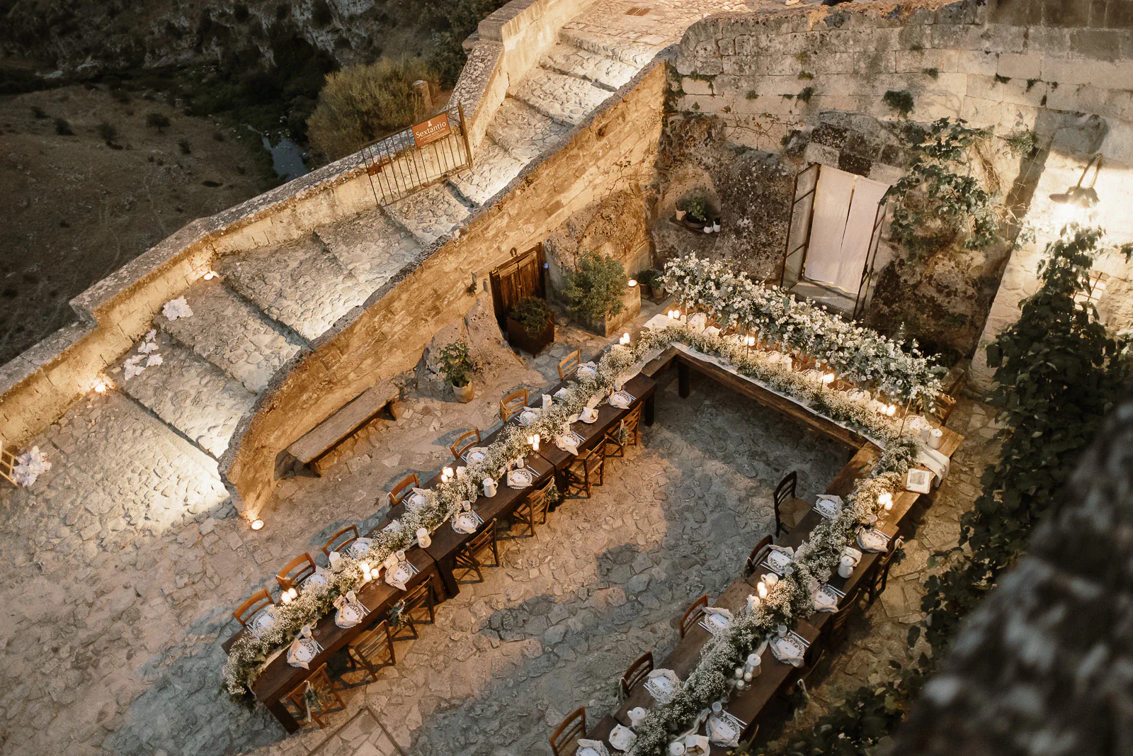 Elegant U-shaped dinner table with white florals graces a rustic stone courtyard in Puglia, perfect for an intimate wedding gathering.