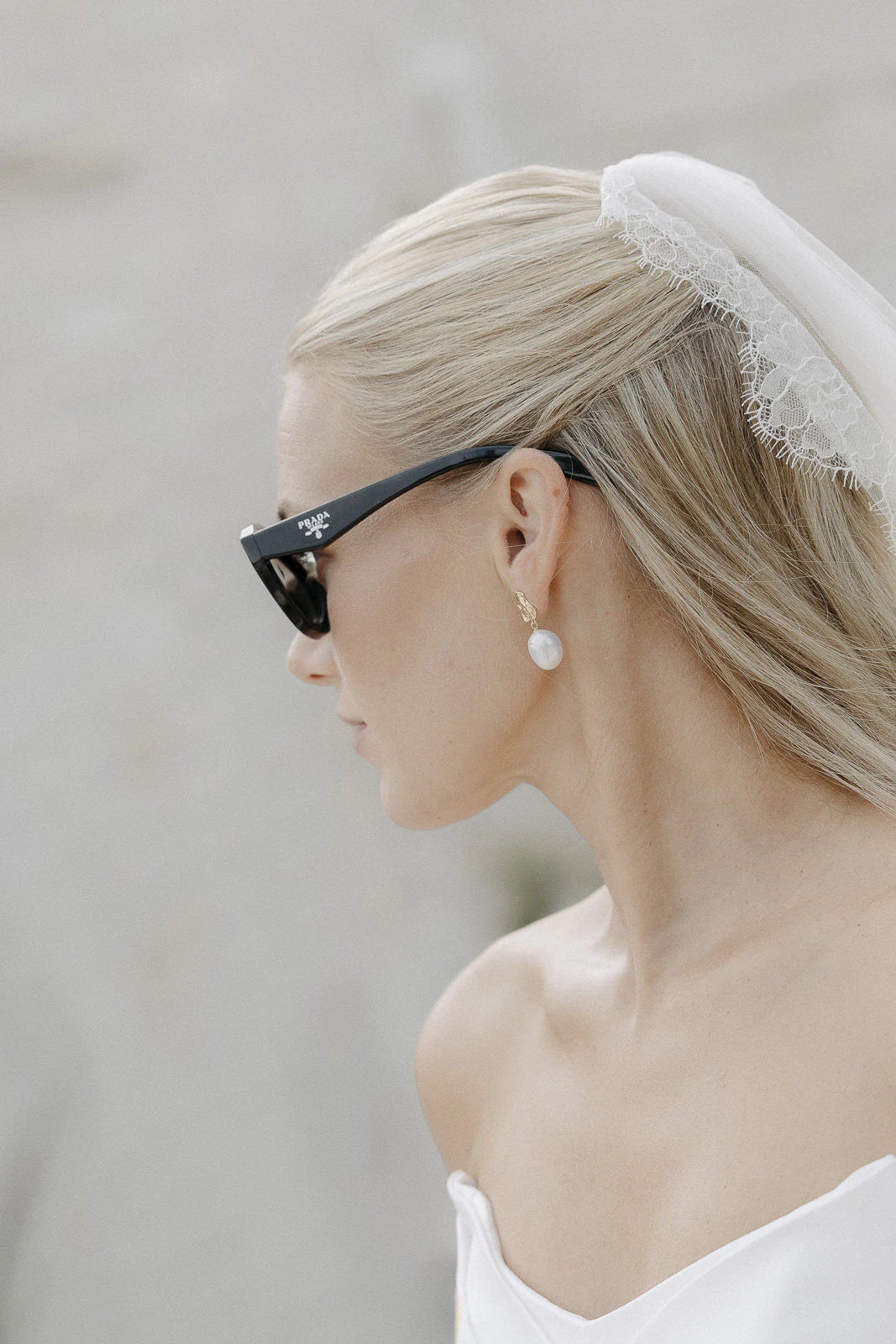 A bride in a chic white gown and veil, pearl earrings and sunglasses, captured in profile—timeless Italian elegance.