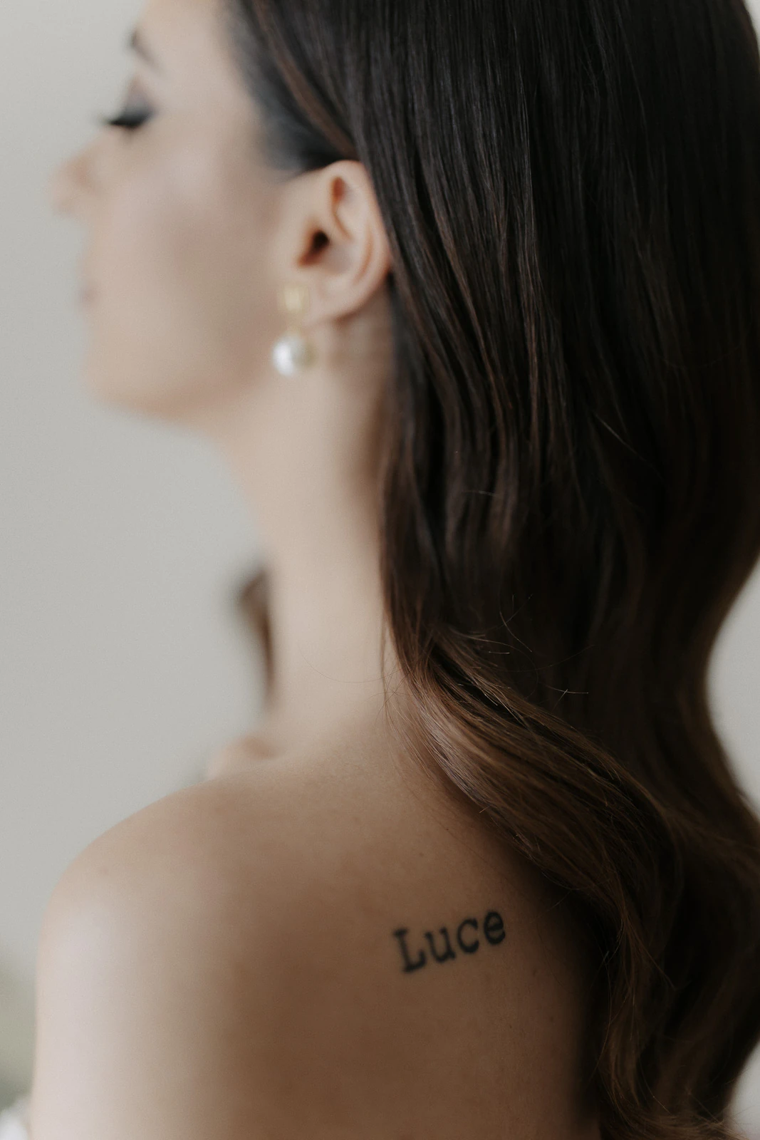Amidst Puglia’s golden light, a bride reveals her Luce tattoo, brown hair softly cascading above pearl earrings.