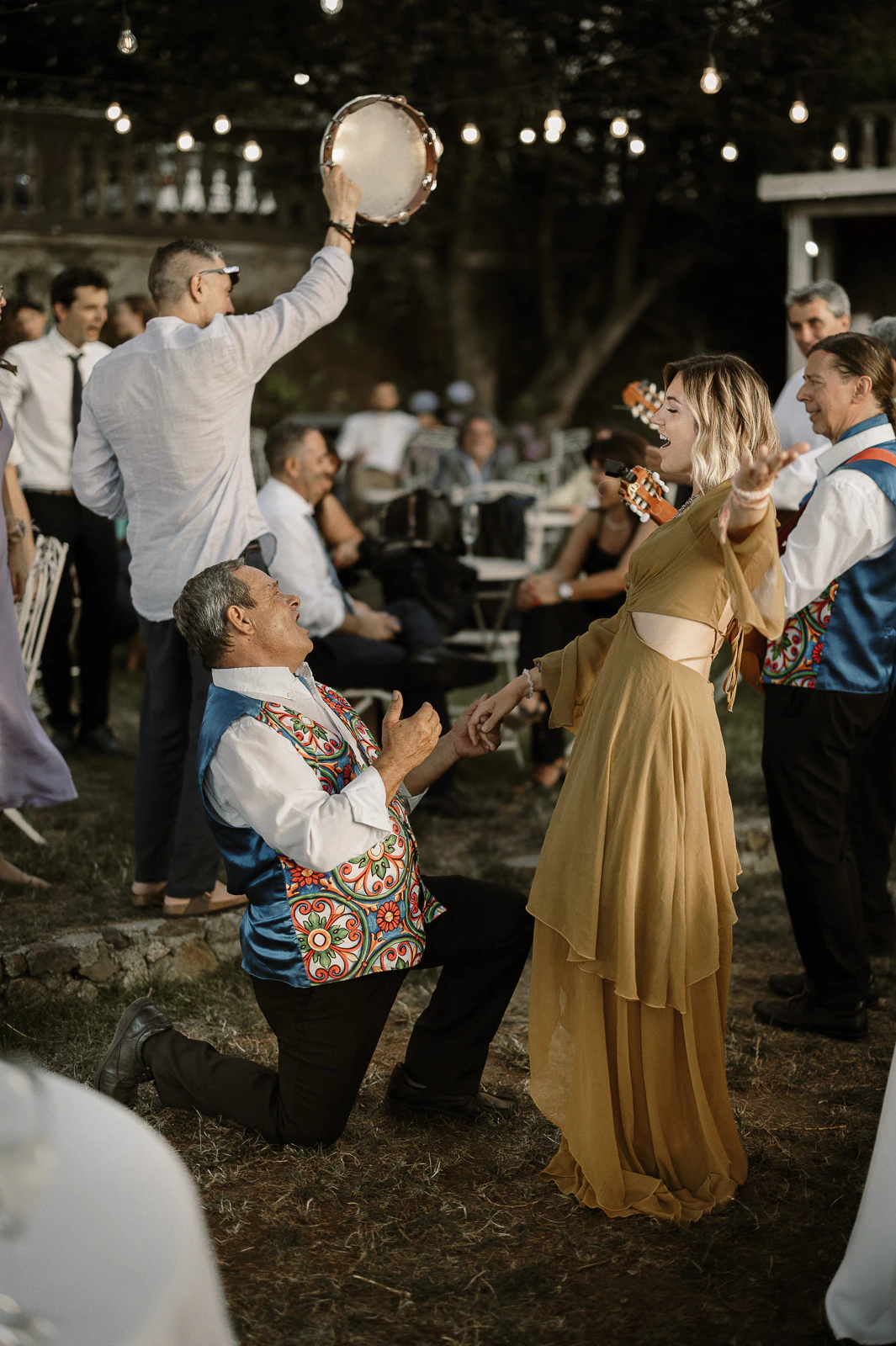 In sunlit Puglia, a joyful couple dance amid laughter and music, guests savoring the romantic Italian ambiance outdoors.