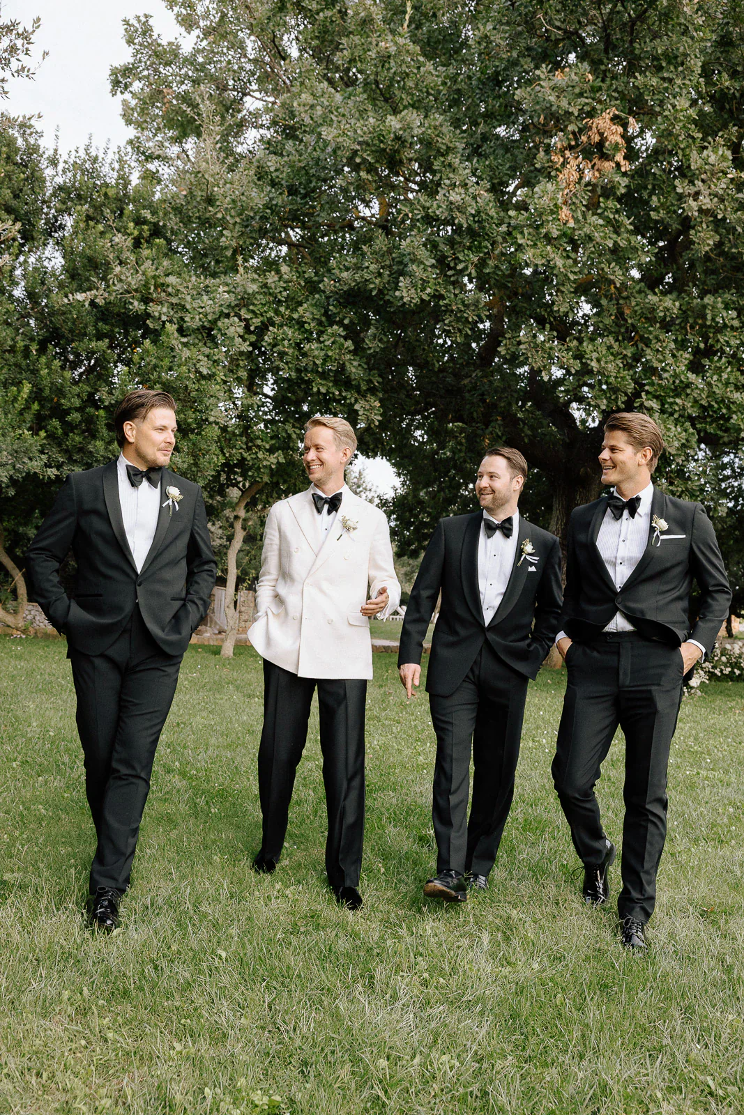 Four groomsmen stroll through sunlit gardens in Puglia, sharing laughter amid the elegance of an Italian destination wedding.