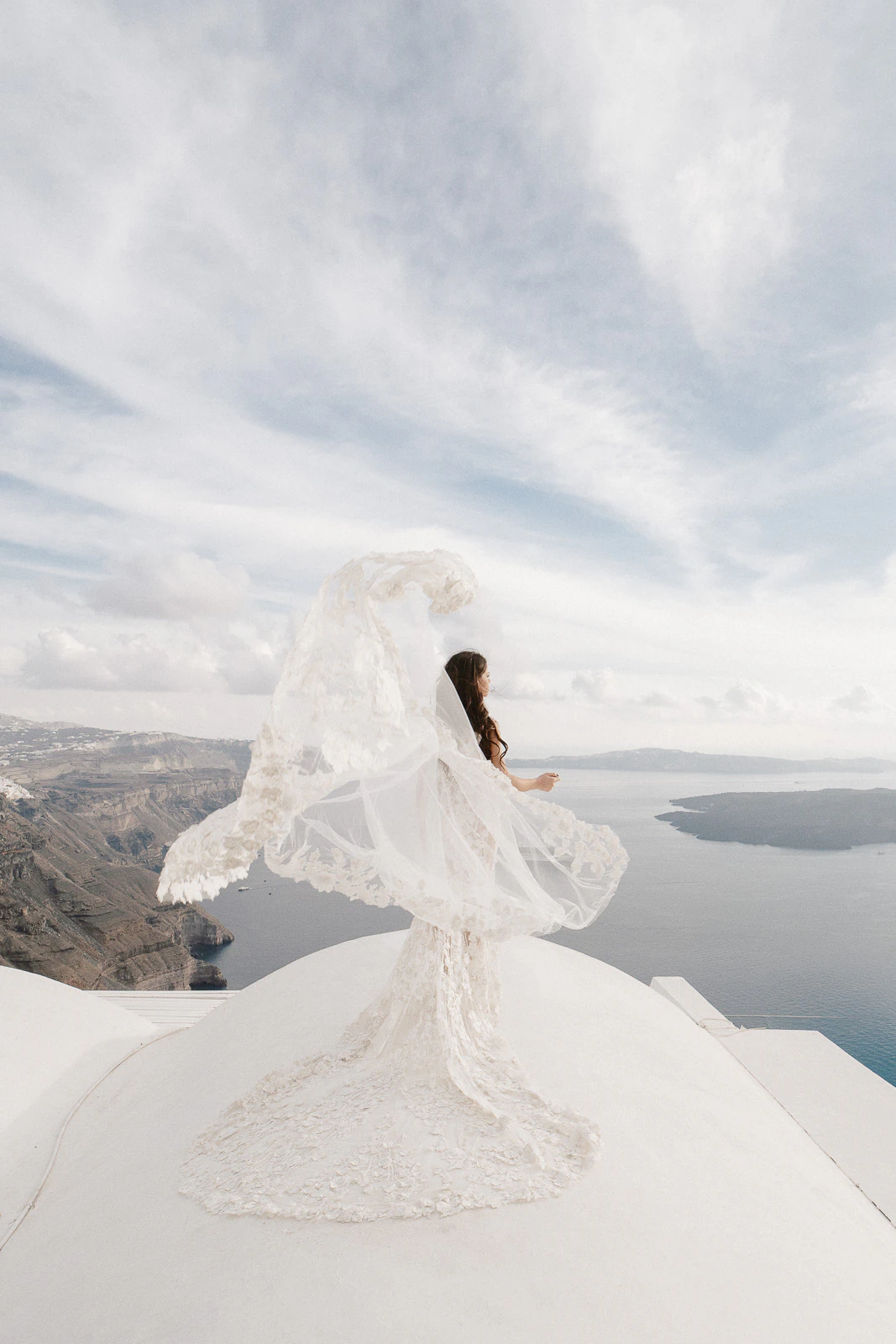 A bride gazes across Puglia’s sunlit coast from a white rooftop, her veil catching the breeze beneath a soft Italian sky.