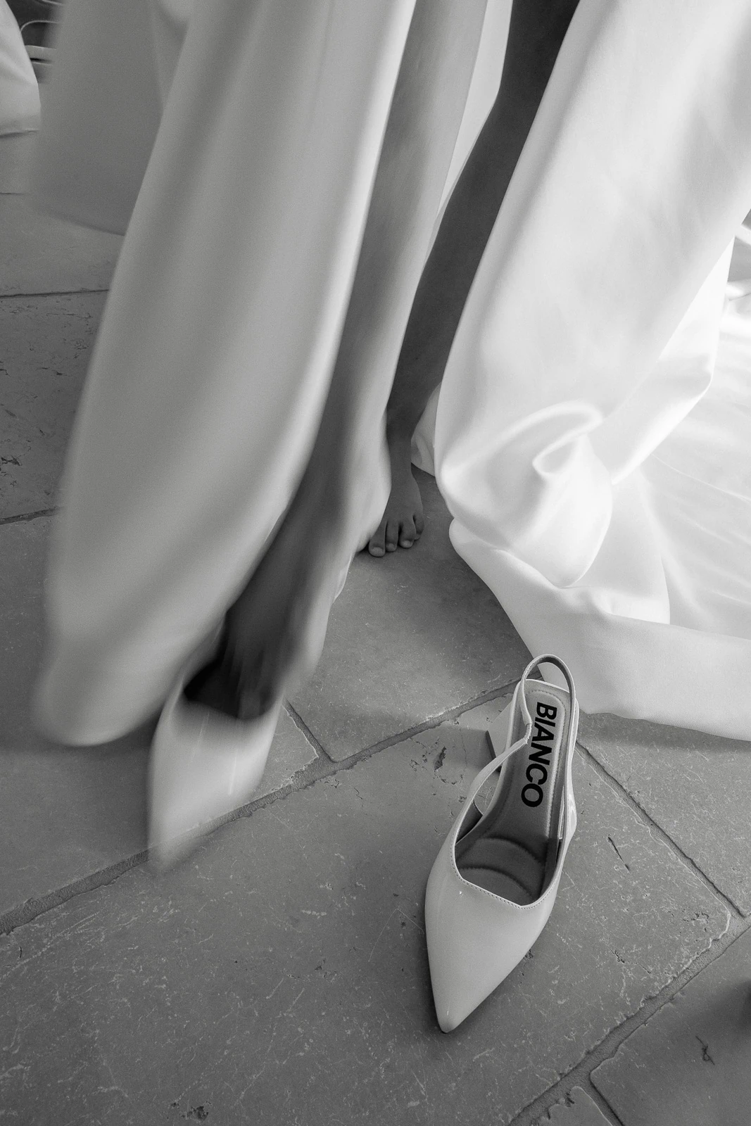 A bride in Puglia gently slips on white Bianco heels, her dress sweeping the sunlit tiles of an Italian villa.