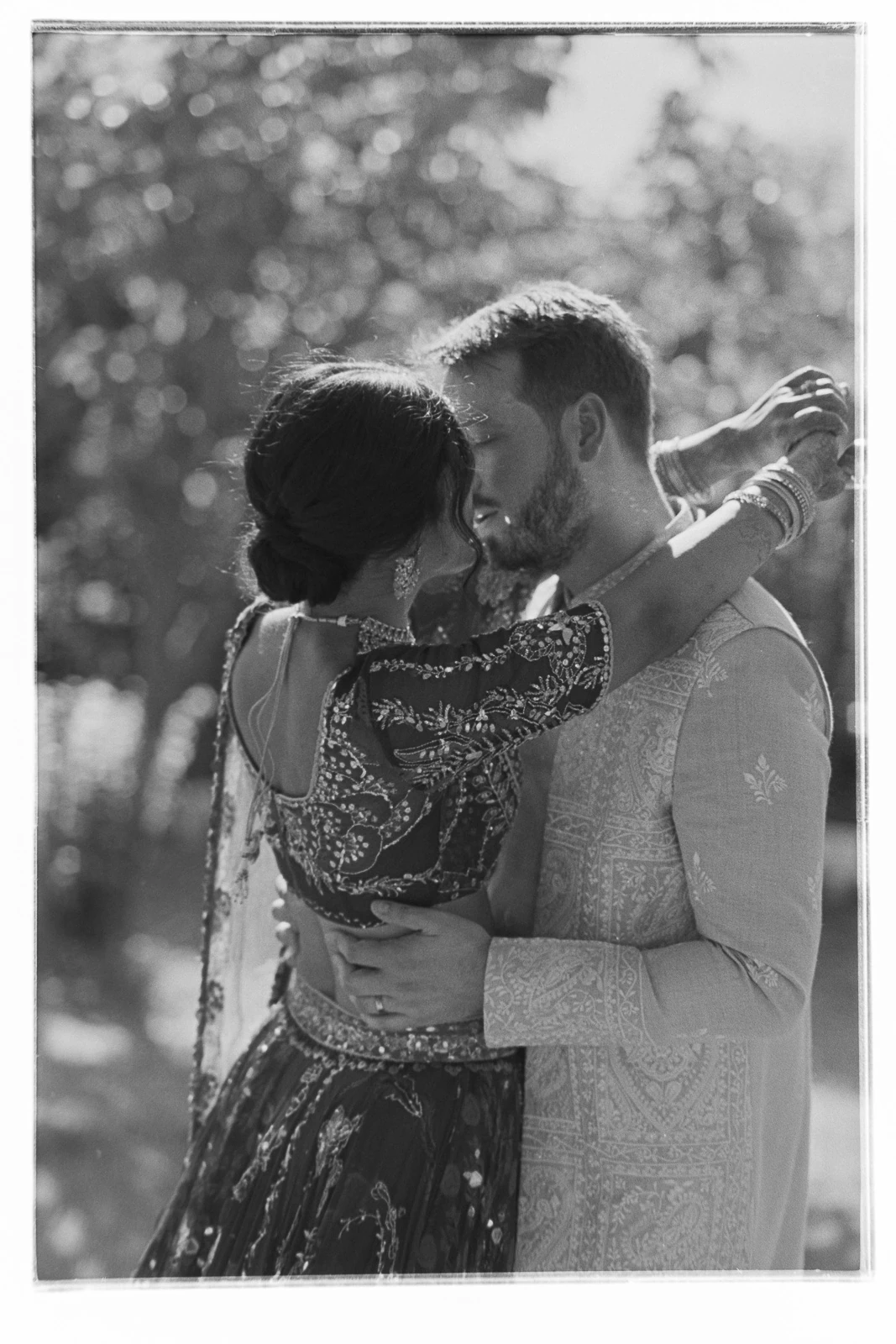 An elegant couple in classic attire shares an intimate embrace under the sunlit skies of Puglia, Italy.