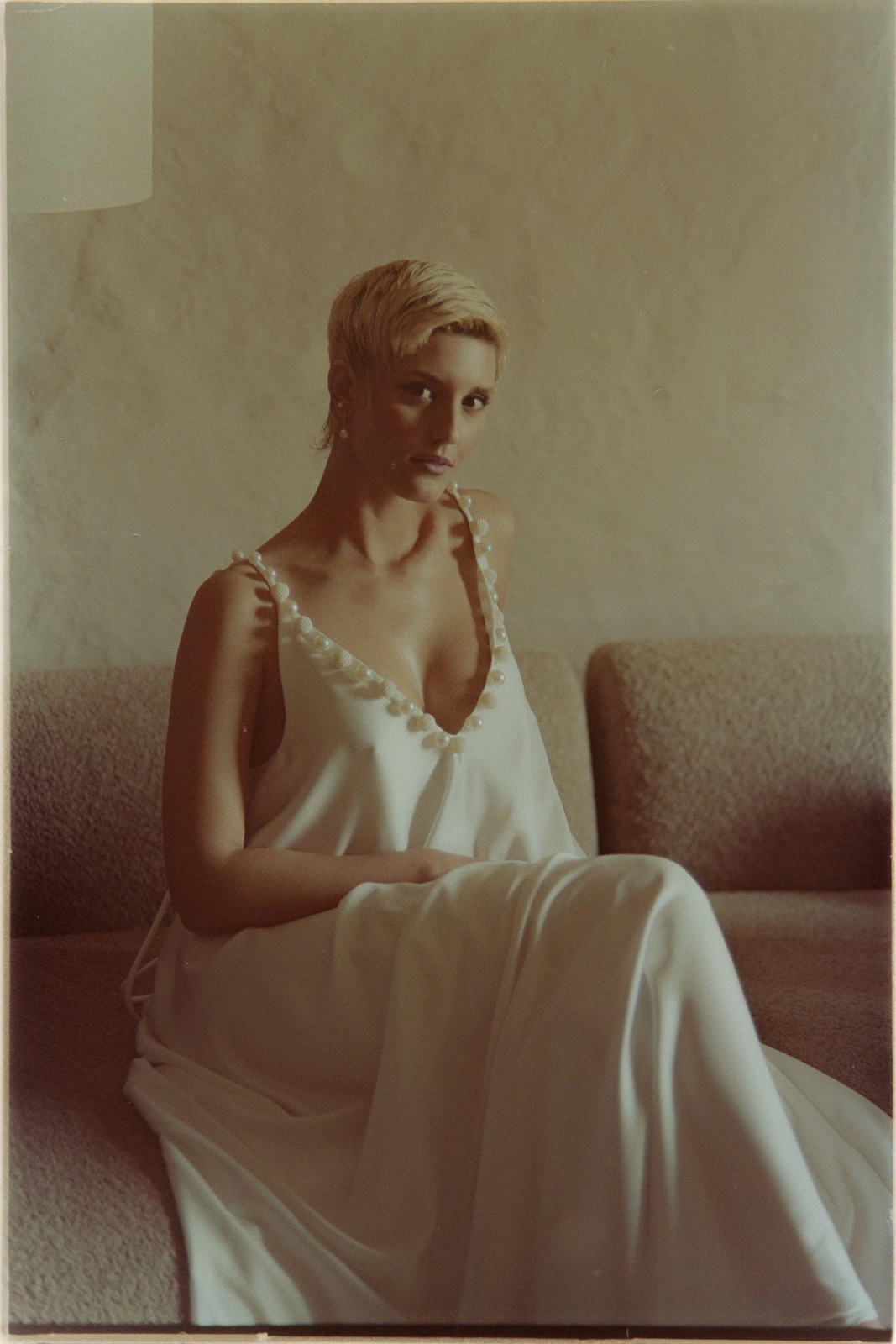 A bride with short blonde hair, in a chic white gown, relaxes on a beige sofa in an elegant Puglia villa.