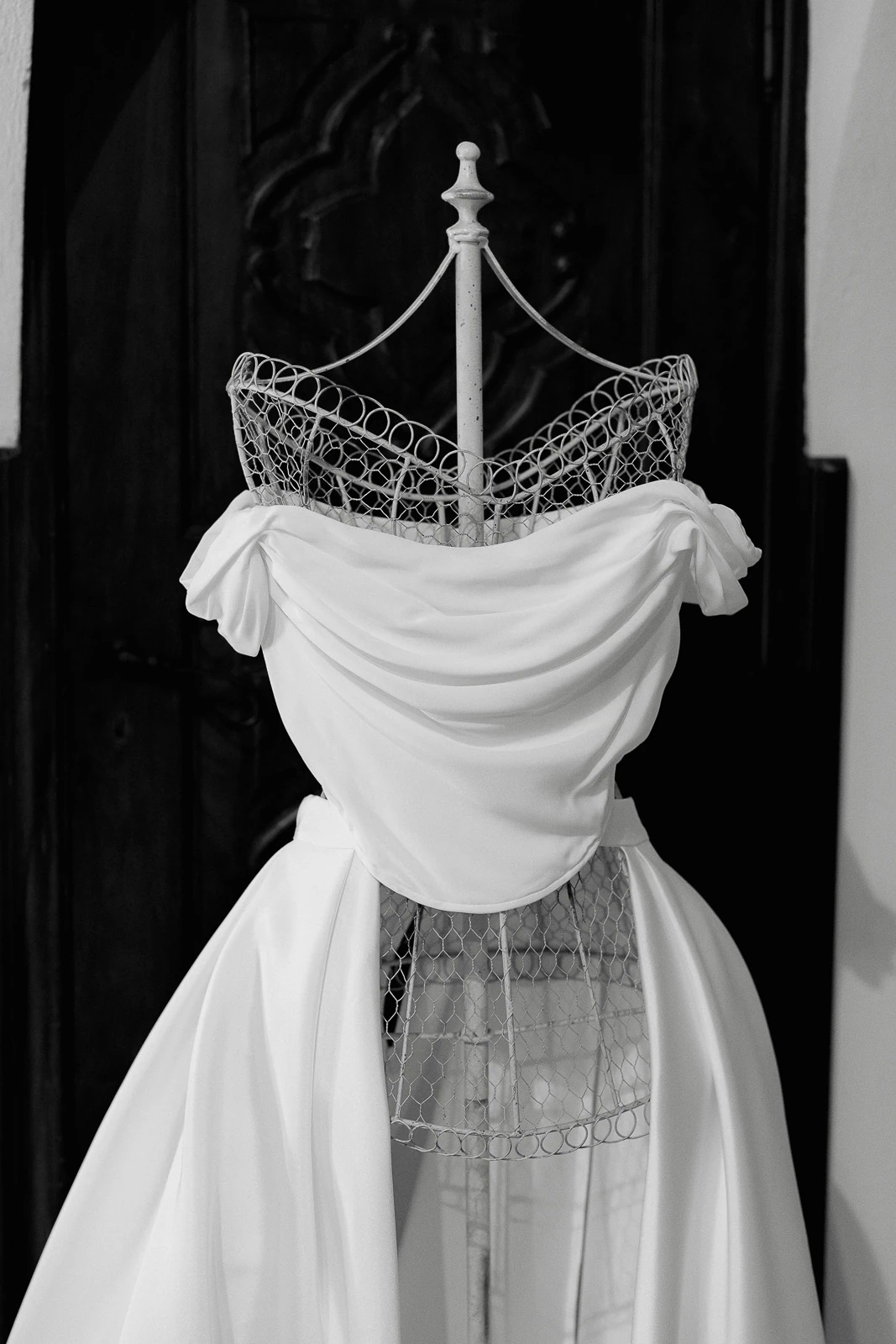 In Puglia, an ethereal off-the-shoulder bridal gown graces a vintage dress form against a rustic wooden door.