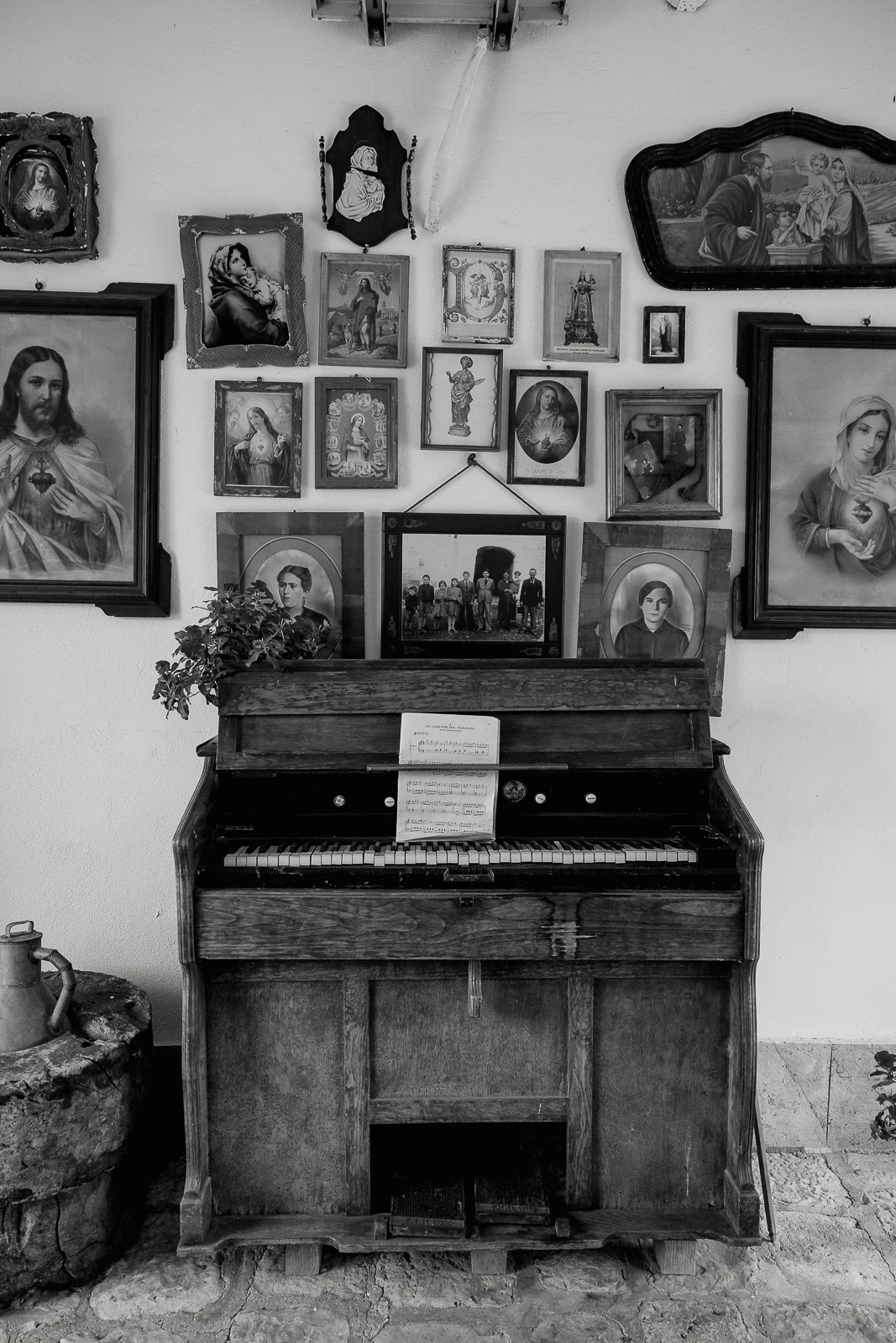 In a sunlit Puglian villa, an antique piano adorned with sheet music stands beneath elegant religious portraits, evoking timeless romance.
