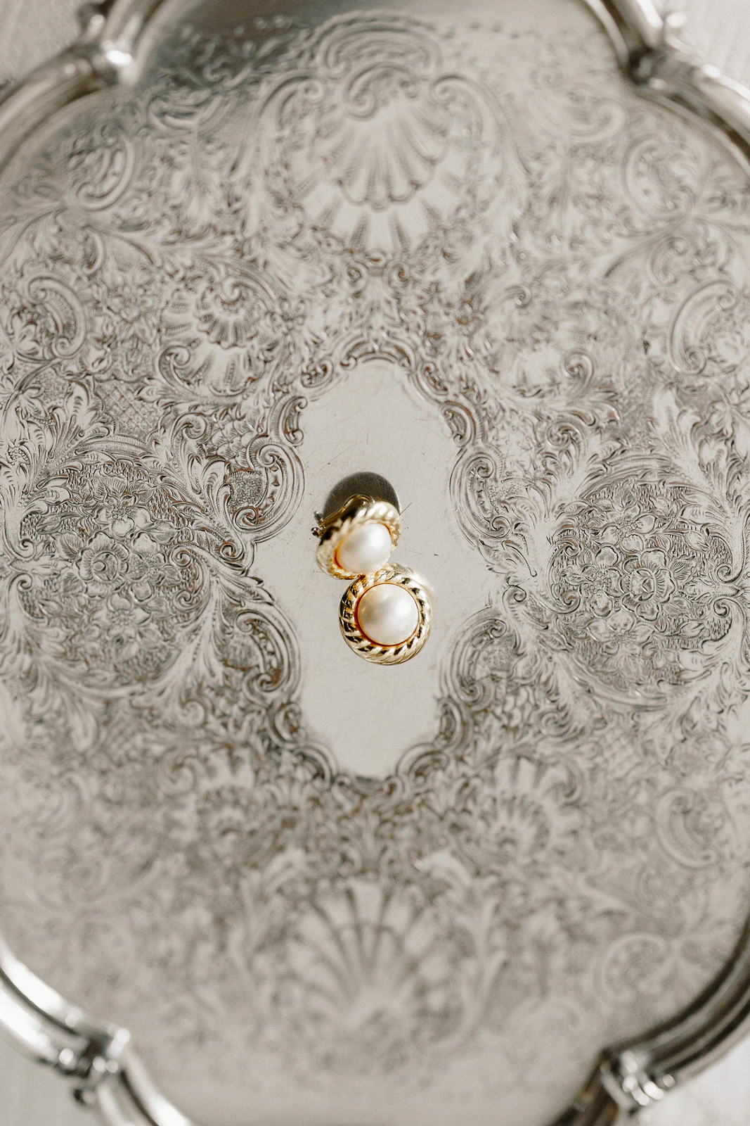 Golden pearl earrings rest atop an intricately engraved silver tray, capturing Puglia’s romance and refined Italian wedding elegance.