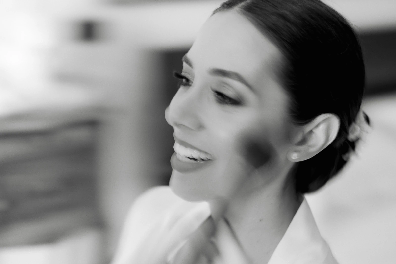 In luminous black and white, a joyful bride in Puglia is softly brushed with makeup before her elegant Italian celebration.