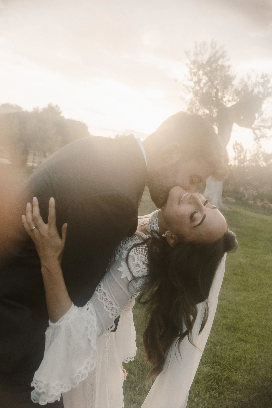 At golden hour in Puglia, a groom tenderly dips and kisses his bride on lush lawns, celebrating love under Italian skies.