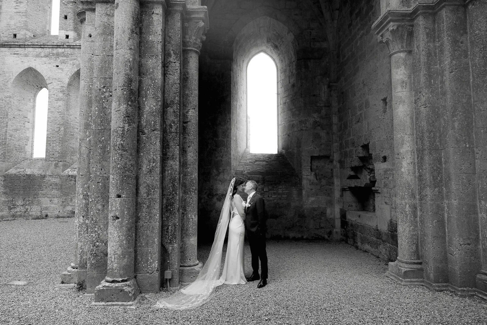 In a historic stone venue in Puglia, the bride and groom share an intimate moment beneath soaring arches and sunlit columns.