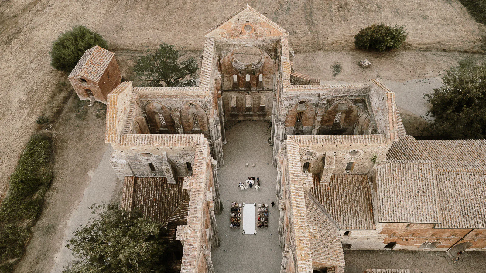 Elegant aerial of guests gathered at a long table in ancient stone ruins, celebrating love amidst Puglia’s golden countryside.