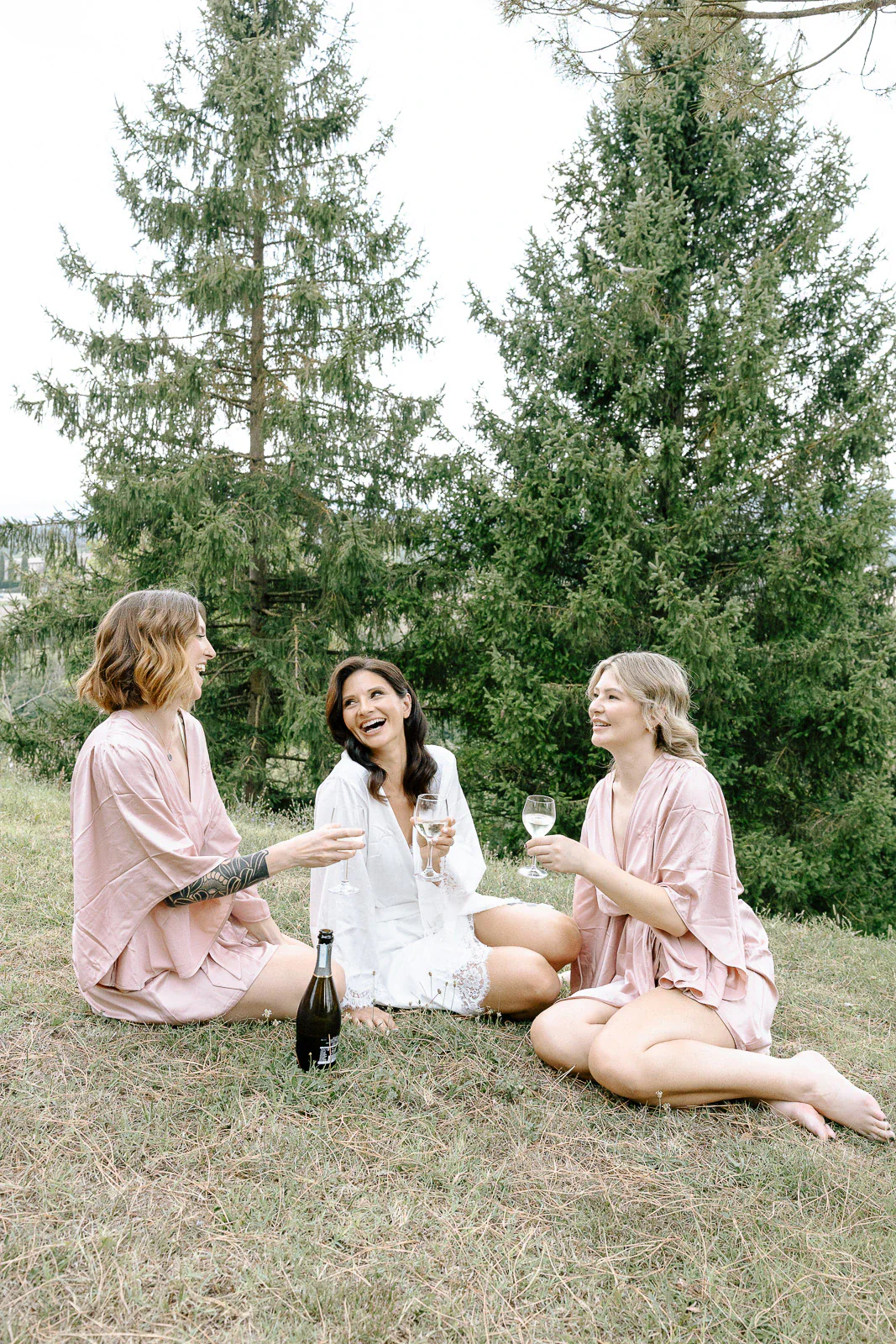 In Puglia, three bridesmaids in robes share laughter and a toast beneath whispering trees—an intimate Italian wedding moment.