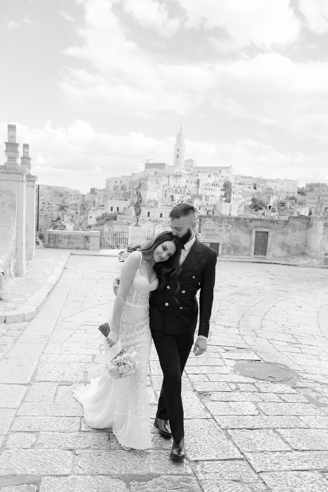 An intimate embrace as the bride and groom stroll a sunlit cobblestone street in Puglia, Italy’s historic heart.
