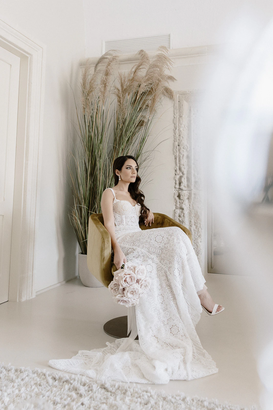 A bride in white lace sits gracefully with pale roses, pampas grass and sunlight evoking effortless romance in Puglia, Italy.