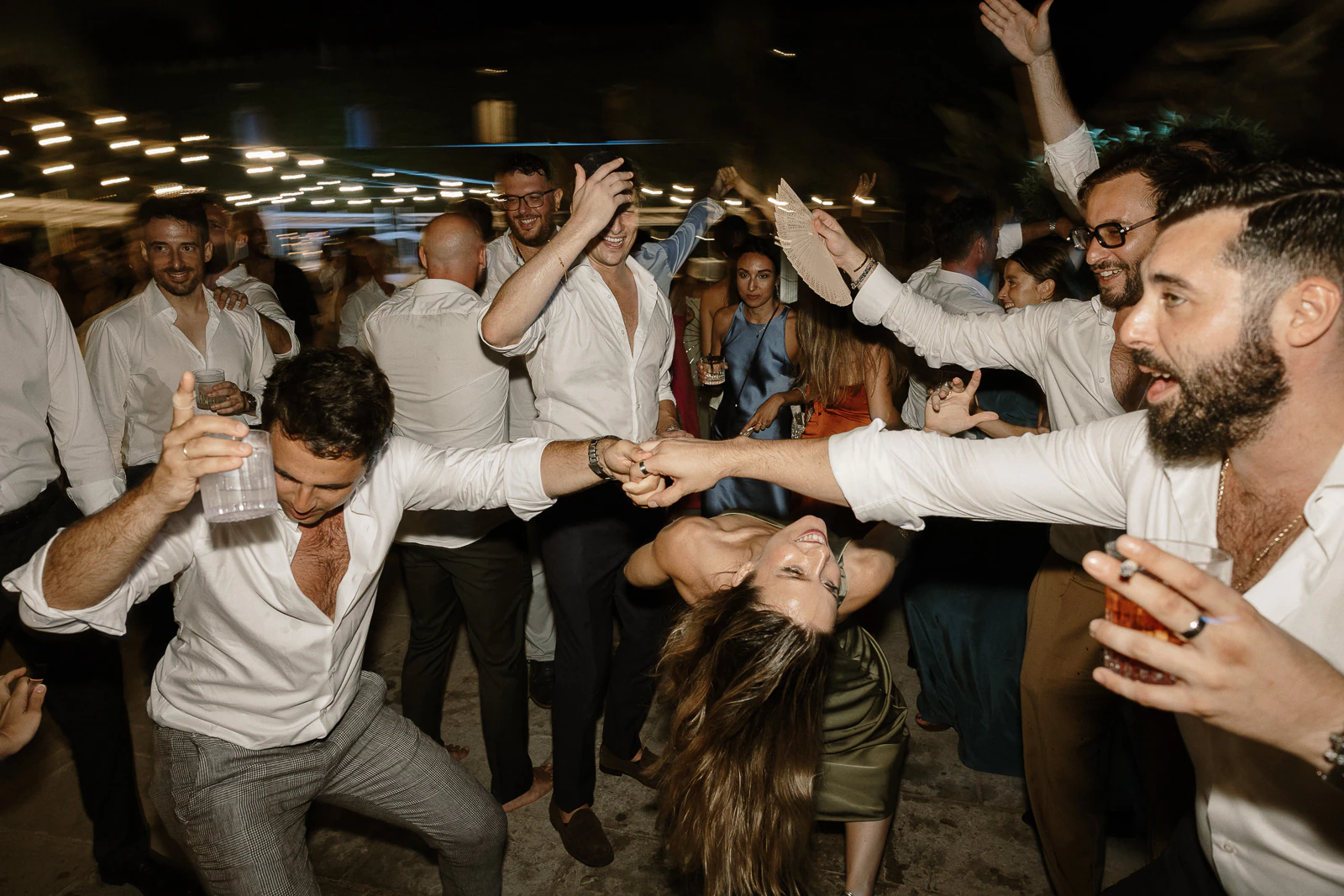 Elegant guests revel beneath glowing string lights at a chic Puglia wedding, their laughter and joy illuminating the night.